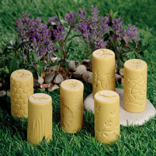 Zes gele yellow door kleistempels met insecten- en tuinpatronen staan in het gras.
