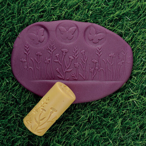 Een gele kleistempel met plantenpatroon ligt naast paarse klei met afdrukken van planten en vlinders.