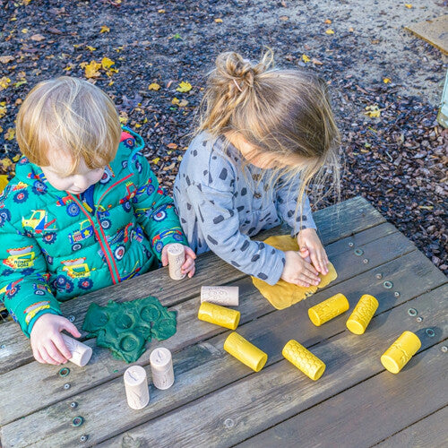 Twee kinderen spelen buiten aan een houten tafel met yellow door kleistempels en klei.