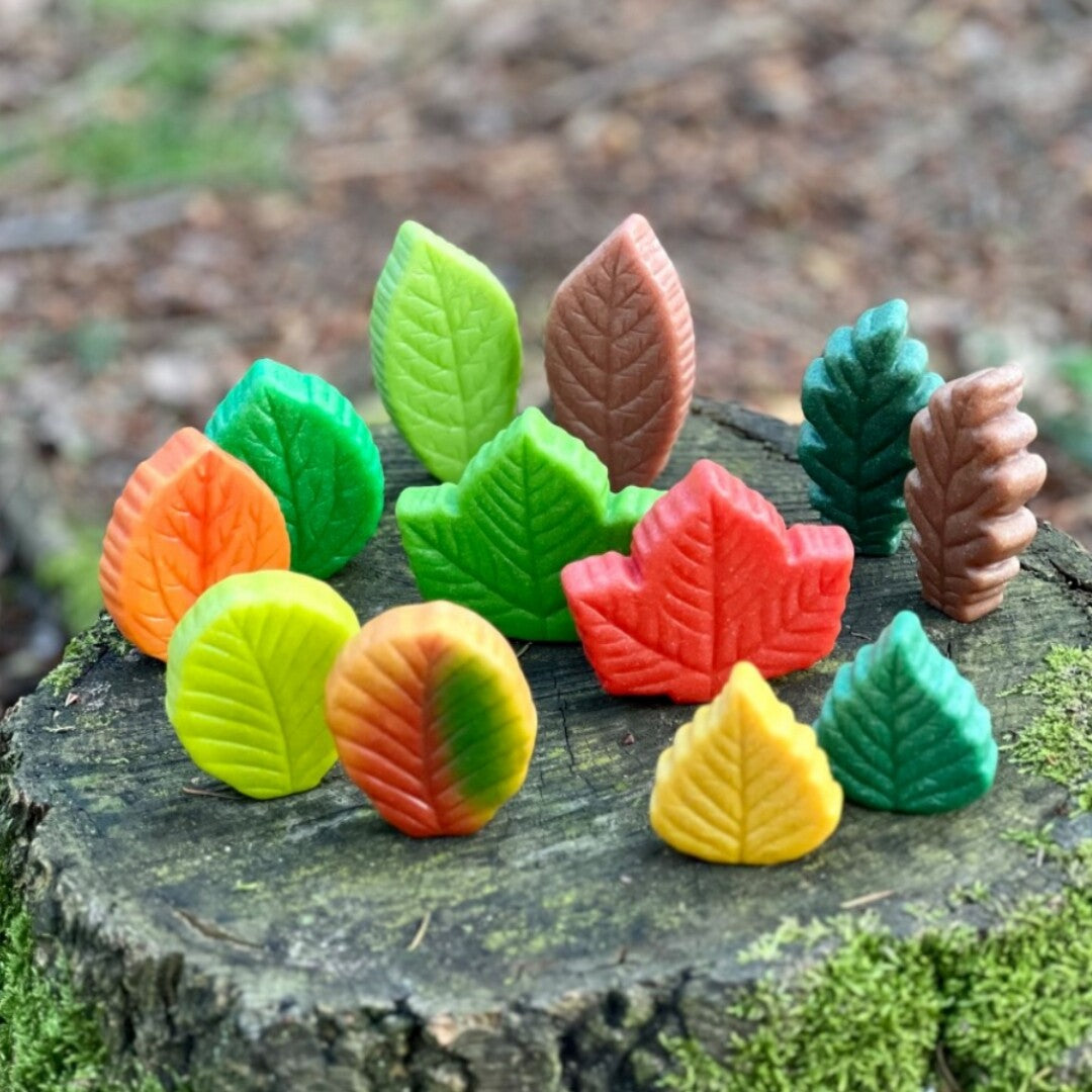 Veelkleurige sensorische speelstenen in de vorm van bladeren, staand op een bemoste boomstronk in het bos.
