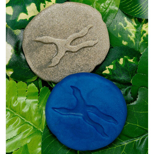 Een speelsteen met een pootafdruk en een blauwe kleiafdruk ervan op groene bladeren.