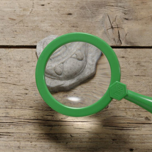 Een groen vergrootglas ligt over een Yellow Door fossiel speelsteen op een houten ondergrond.
