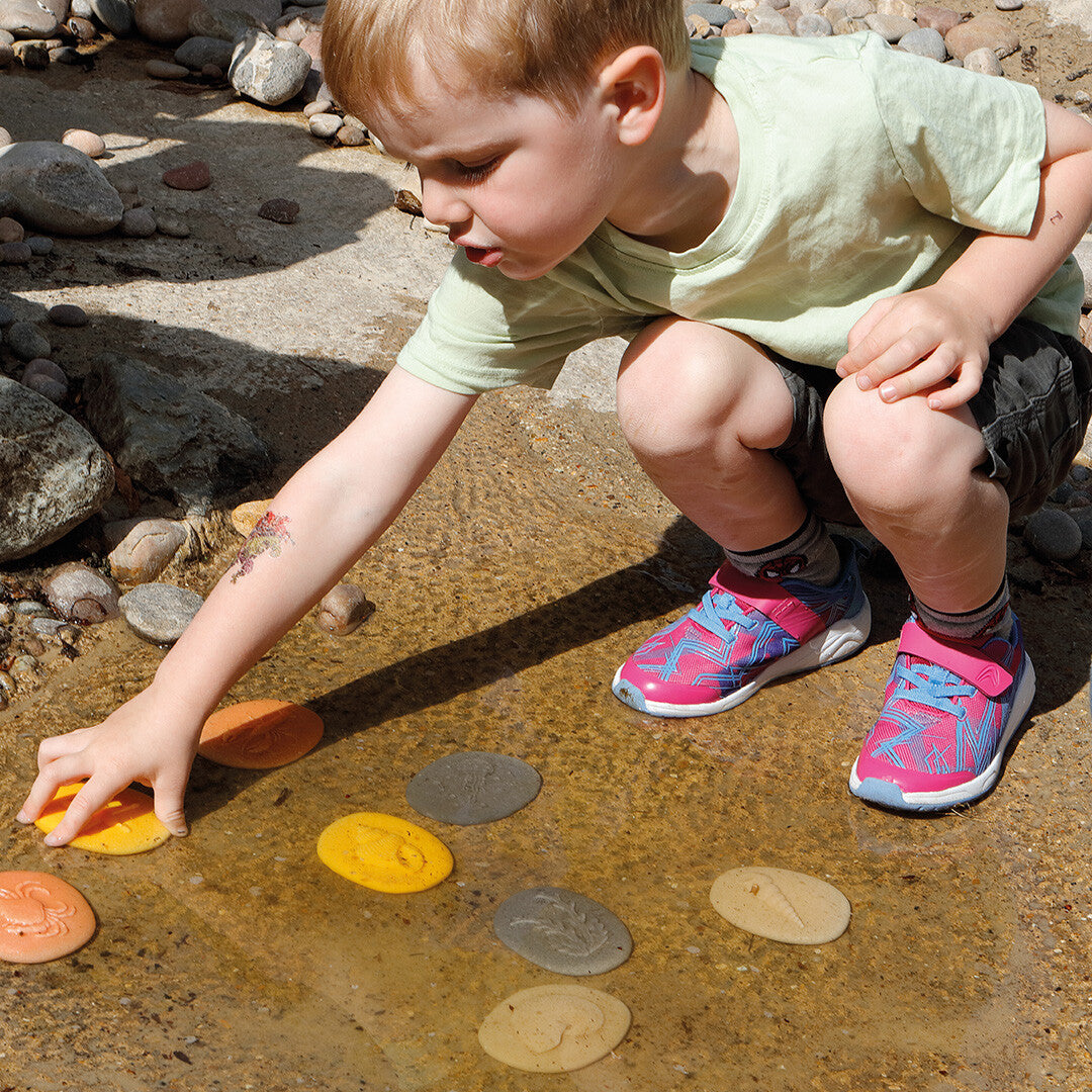 Een kind speelt met de kustthema speelstenen in ondiep water.