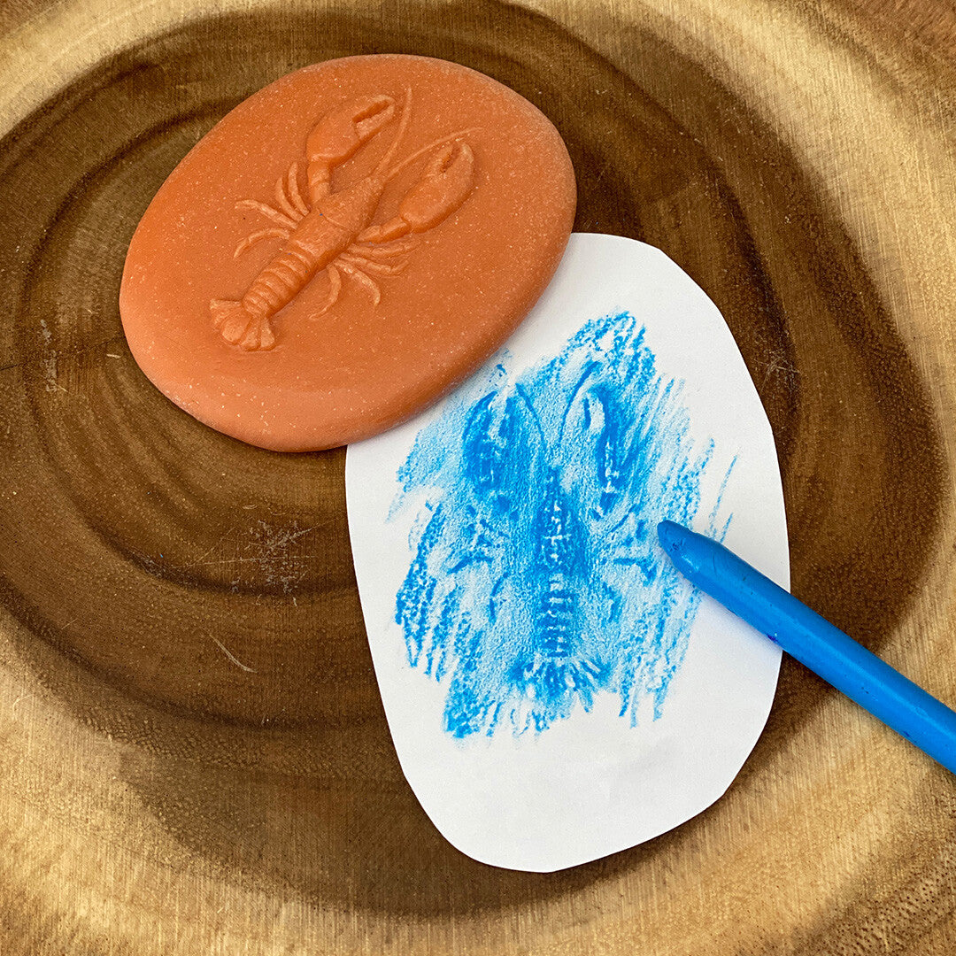 Een oranje speelsteen met kreeftpatroon en een blauwe krijttekening van de kreeft op papier.
