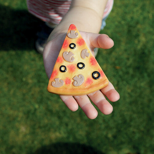 Een kinderhand houdt een pizza-vormige sensorische speelsteen vast boven gras.