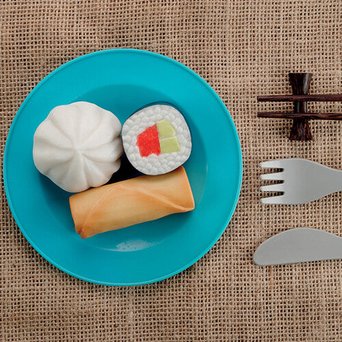 Een blauw bord met een dumpling, sushi en loempia speelsteen, naast speelgoedbestek en eetstokjes.