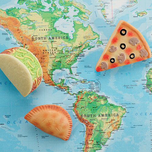 Drie 'Foods of the World' sensorische speelstenen, een taco, pizza en empanada, liggen op een wereldkaart.