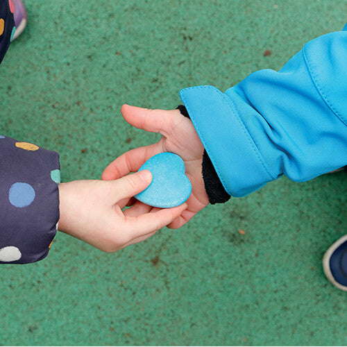 Twee kinderhanden wisselen een blauwe hartvormige sensorische steen uit boven een groene ondergrond.