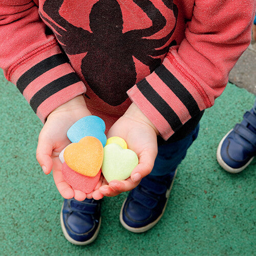 Kinderhanden houden een handvol veelkleurige hartvormige sensorische stenen vast.