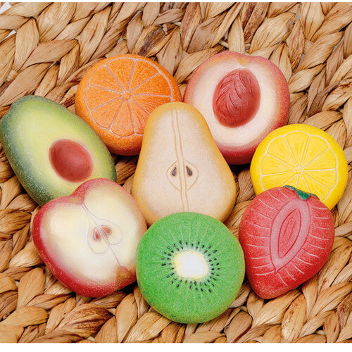 Acht Yellow Door stenen speelfruitstukken, waaronder een halve perzik, kiwi en avocado, liggen op een gevlochten mat.
