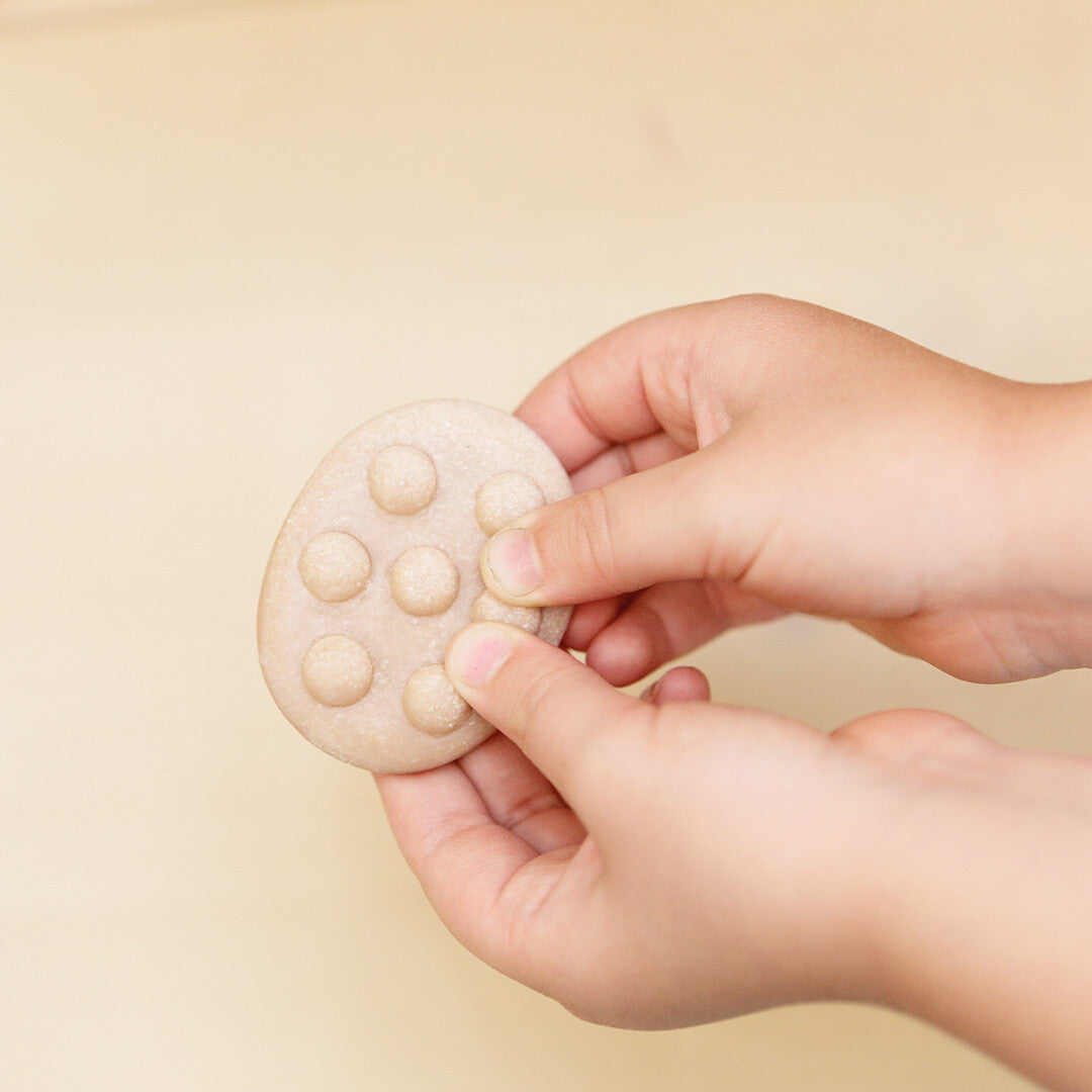 Twee kinderhanden voelen aan een ovaalvormige Yellow Door vinger fidget steen met textuur van bolletjes.