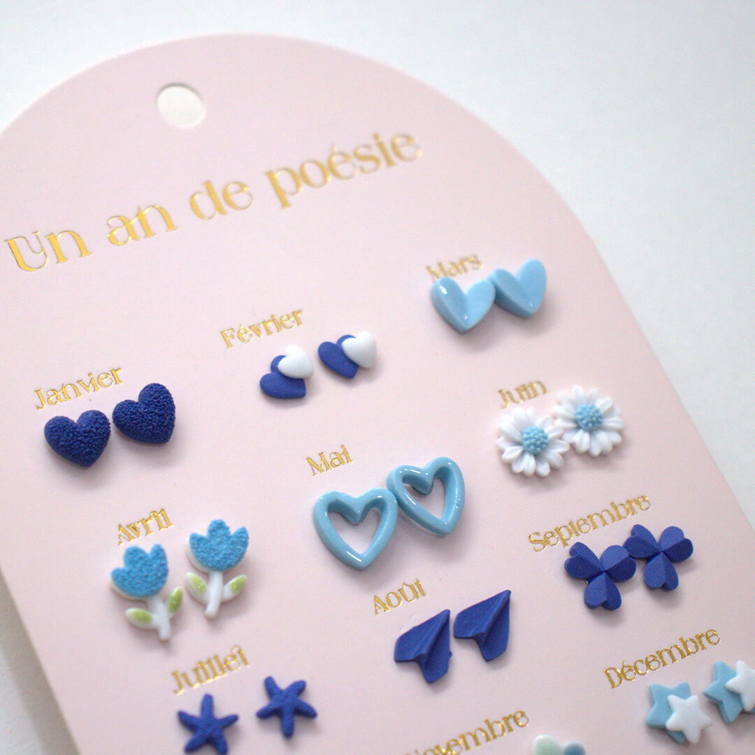 Detailopname van een set kinder oorbellen met blauwe oorknopjes in de vorm van harten, bloemen en andere figuren.
