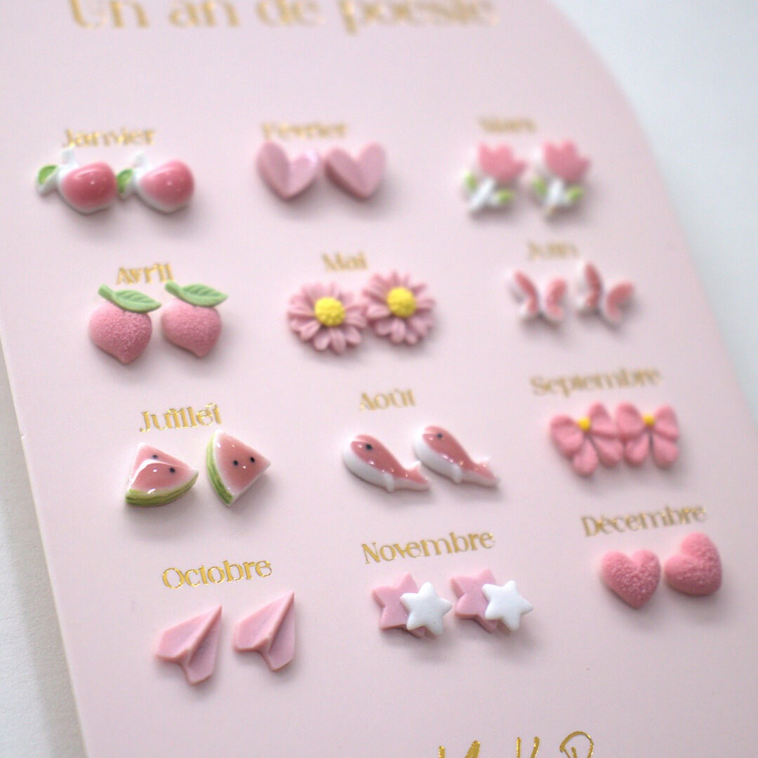 Detailopname van de Yuko B. kinder oorbellen set met roze oorknopjes in de vormen van appels, harten, bloemen, vlinders, watermeloen, vissen, strikjes, papieren vliegtuigjes en sterren.