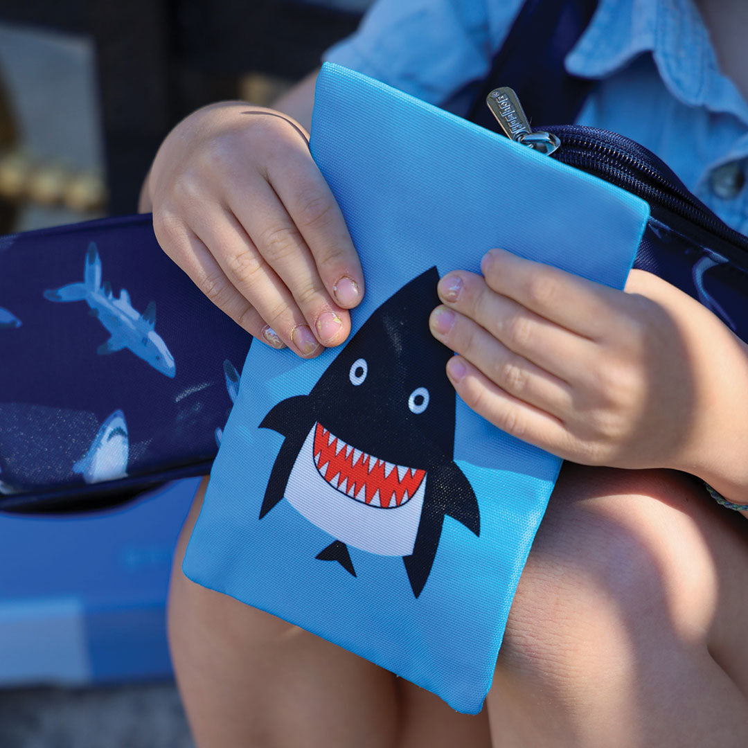 Een kind houdt een blauw Yumbox koelelement met haaienprint vast.