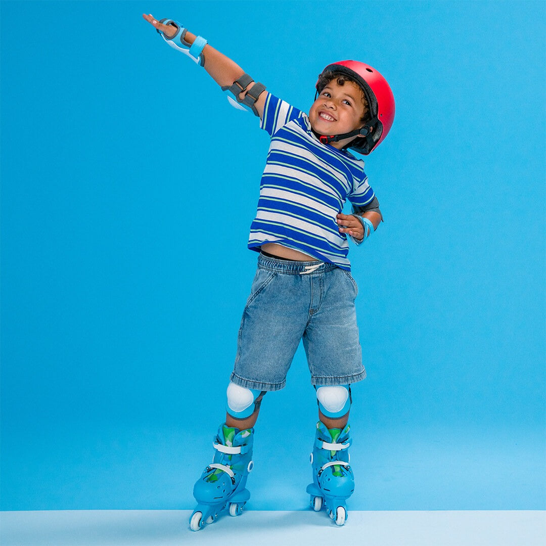 Een lachende jongen draagt blauwe Yvolution kinderskeelers, een rode helm en beschermers, staand op een blauwe achtergrond.