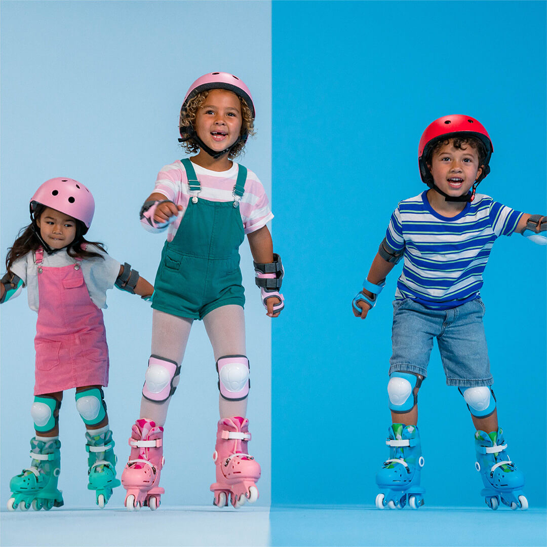 Drie kinderen dragen verschillende kleuren kinderskeelers en beschermende kleding, staand op een tweekleurige achtergrond.