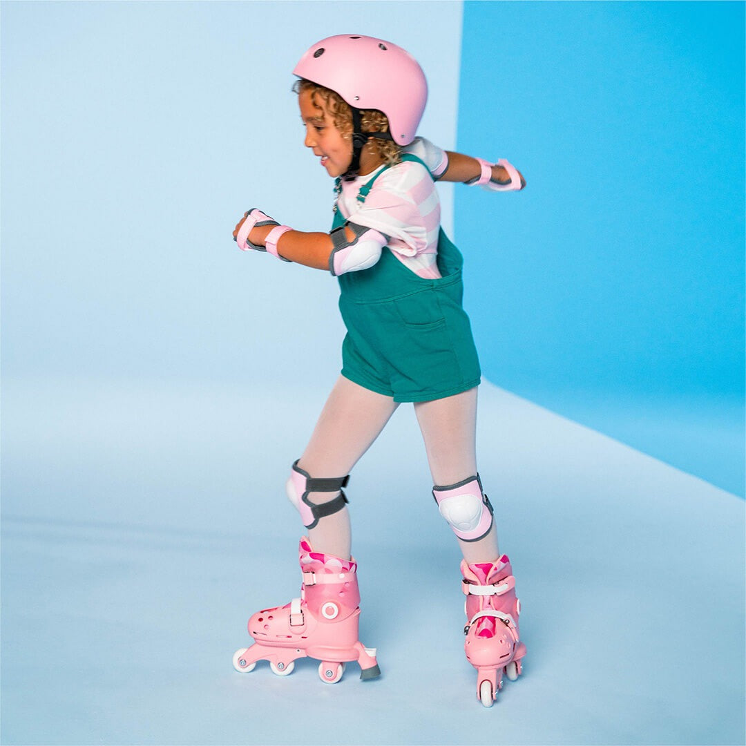 Een kind met roze Yvolution kinderskeelers, een roze helm en beschermers, lachend aan het skeeleren.