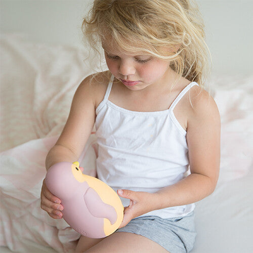 Een jong meisje zit op bed en houdt de roze Zazu pinguïn slaaptrainer vast.