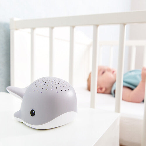 Zazu grijze walvis muziekdoos en lichtprojector op een nachtkastje naast een babybedje.