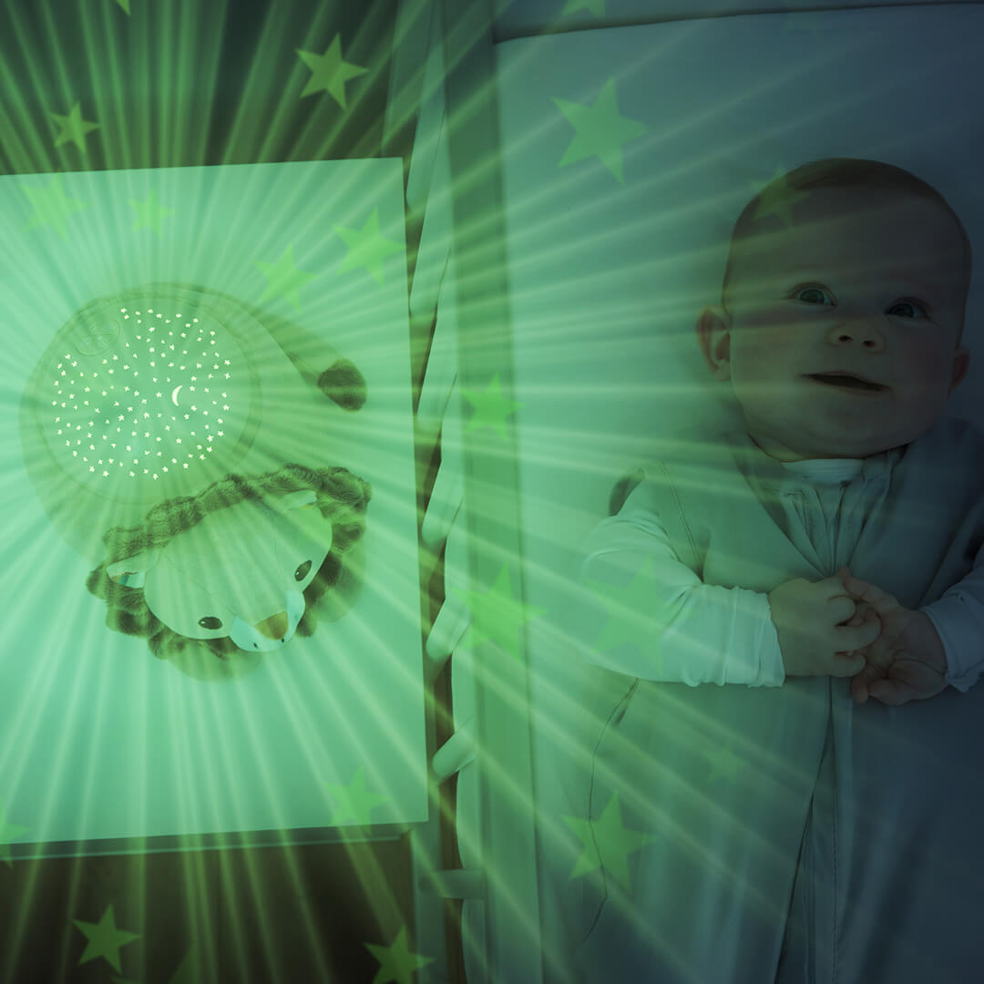 Een baby ligt in een wieg met groene sterren geprojecteerd door de Zazu leeuw sterprojector.
