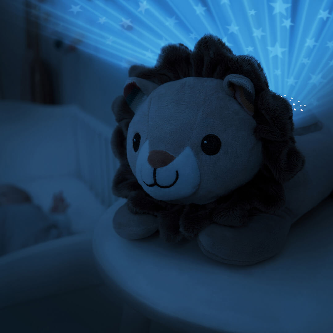 De Zazu leeuw sterprojector projecteert blauwe sterren op de muur naast een babywieg.