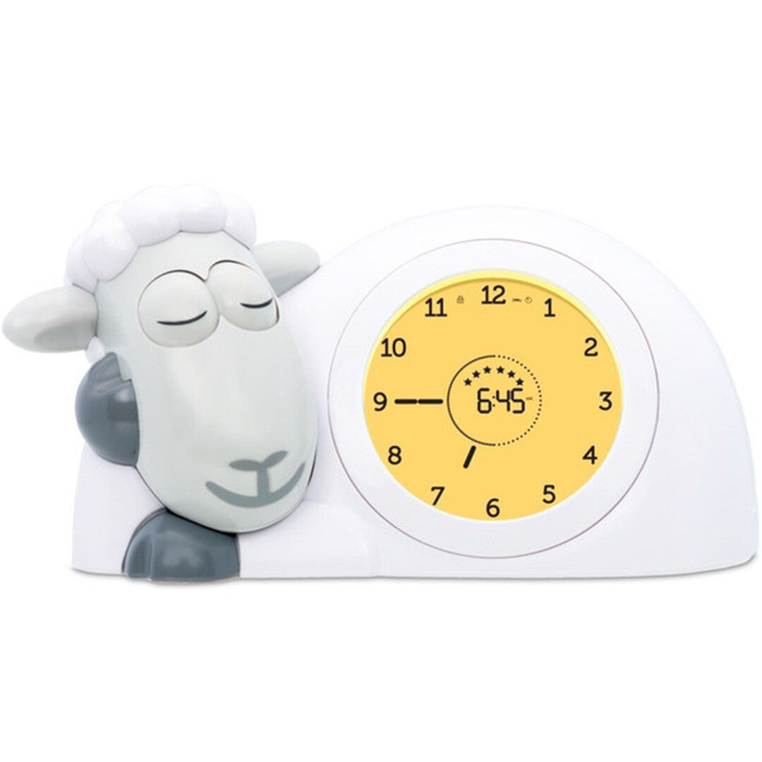 Zazu slaaptrainer en wekker in de vorm van een schaap met grijs gezicht en gesloten ogen, de klok toont 6:45 met een gele achtergrond.
