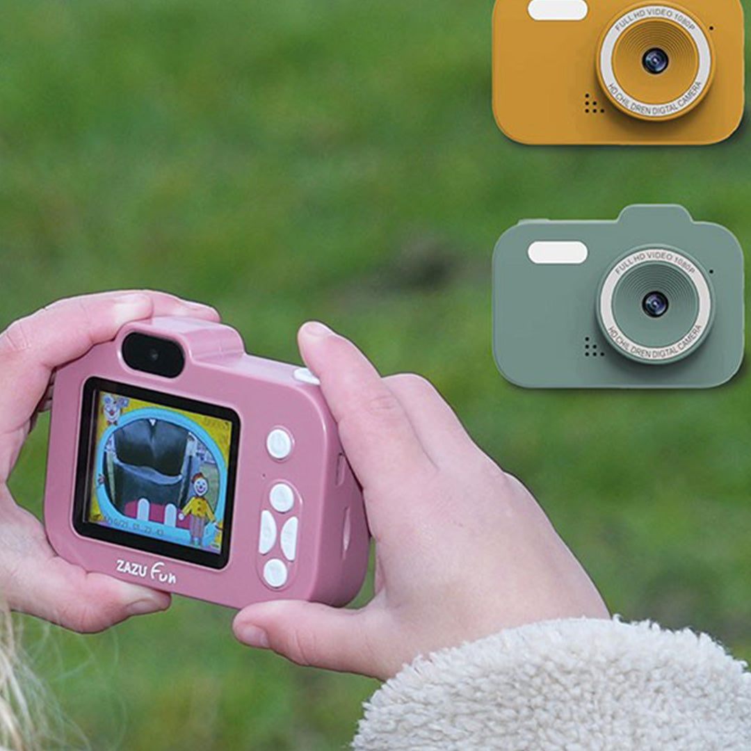 Kind houdt een roze Zazu digitale kindercamera vast, met gele en groene camera's op de achtergrond.