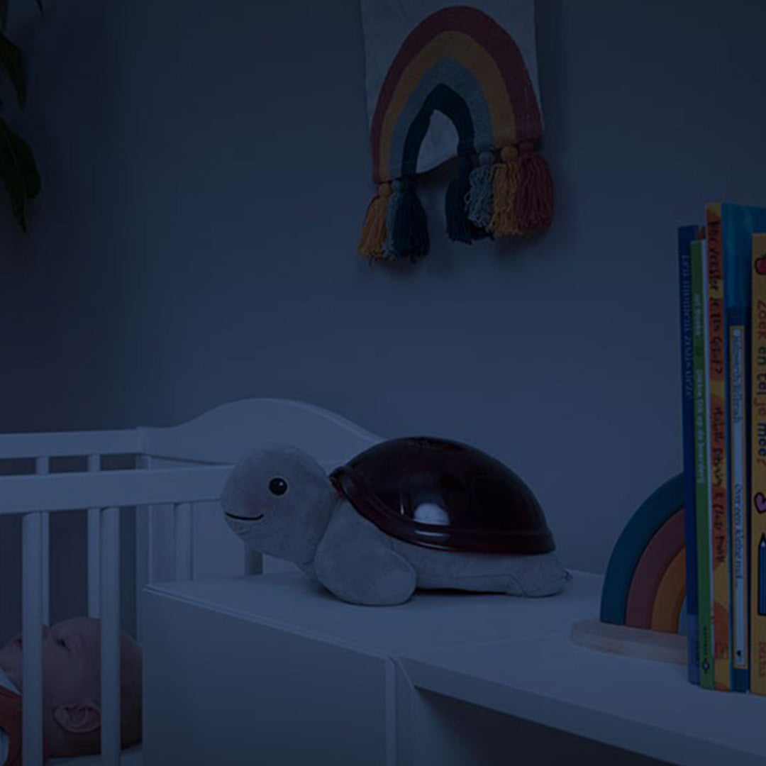 Zazu Tim de schildpad muziekdoos en lichtprojector op een plank naast een babybedje in een donkere kamer.