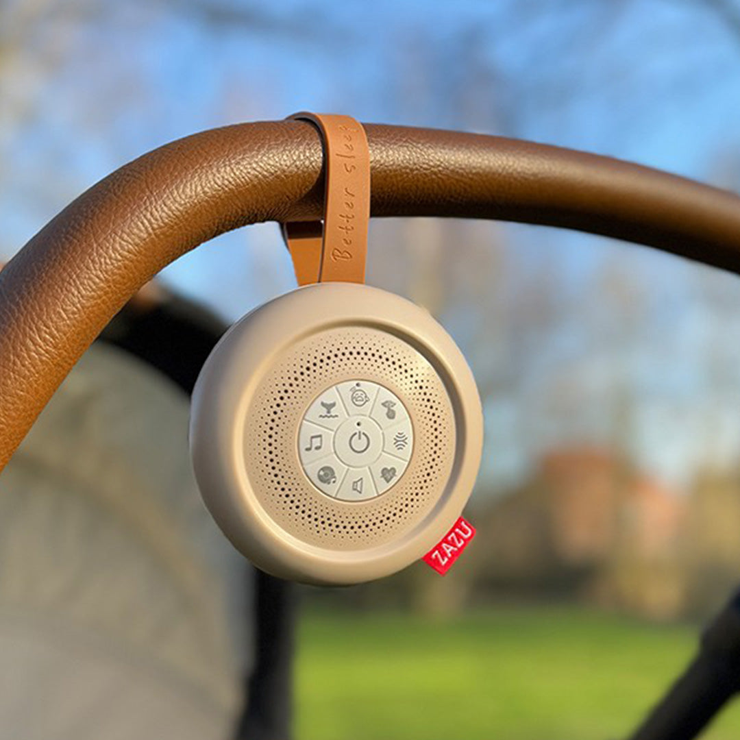 Zazu beige geluidsmachine hangend aan de bruine duwstang van een kinderwagen.