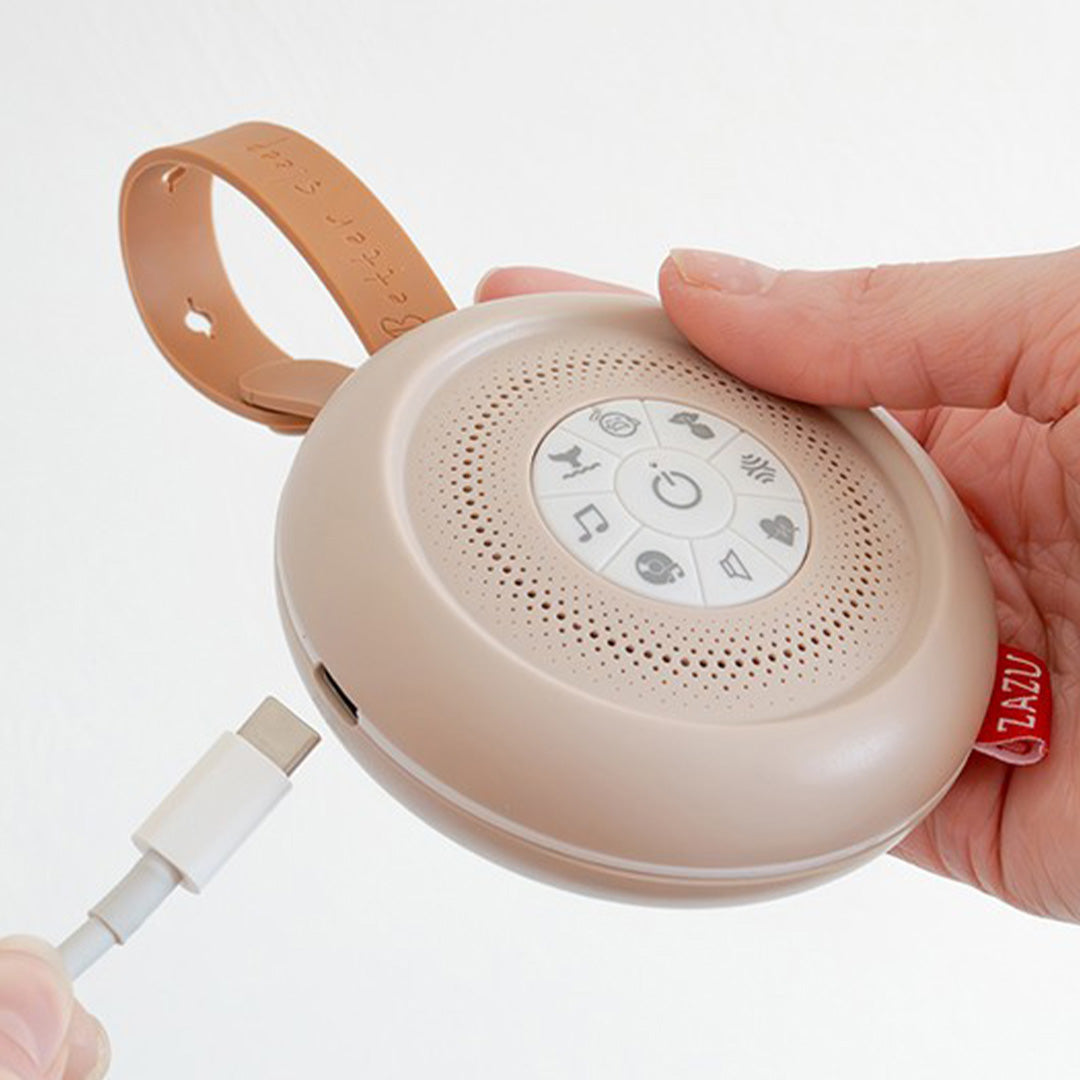 Een hand steekt een USB-C kabel in de Zazu beige geluidsmachine.